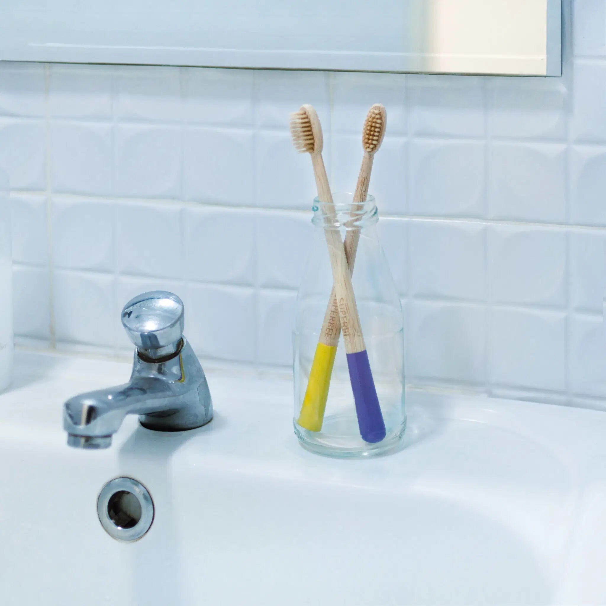 SuperBee Australia bamboo toothbrushes with yellow and purple handles in a glass jar on a bathroom sink