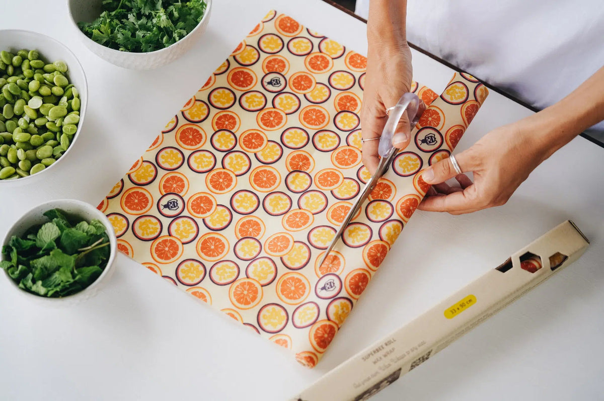 SuperBee Australia beeswax wrap roll with passion fruit print being cut with scissors on a white kitchen table