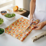 SuperBee Australia beeswax wrap roll with orange and passion fruit print being cut with scissors on a kitchen counter