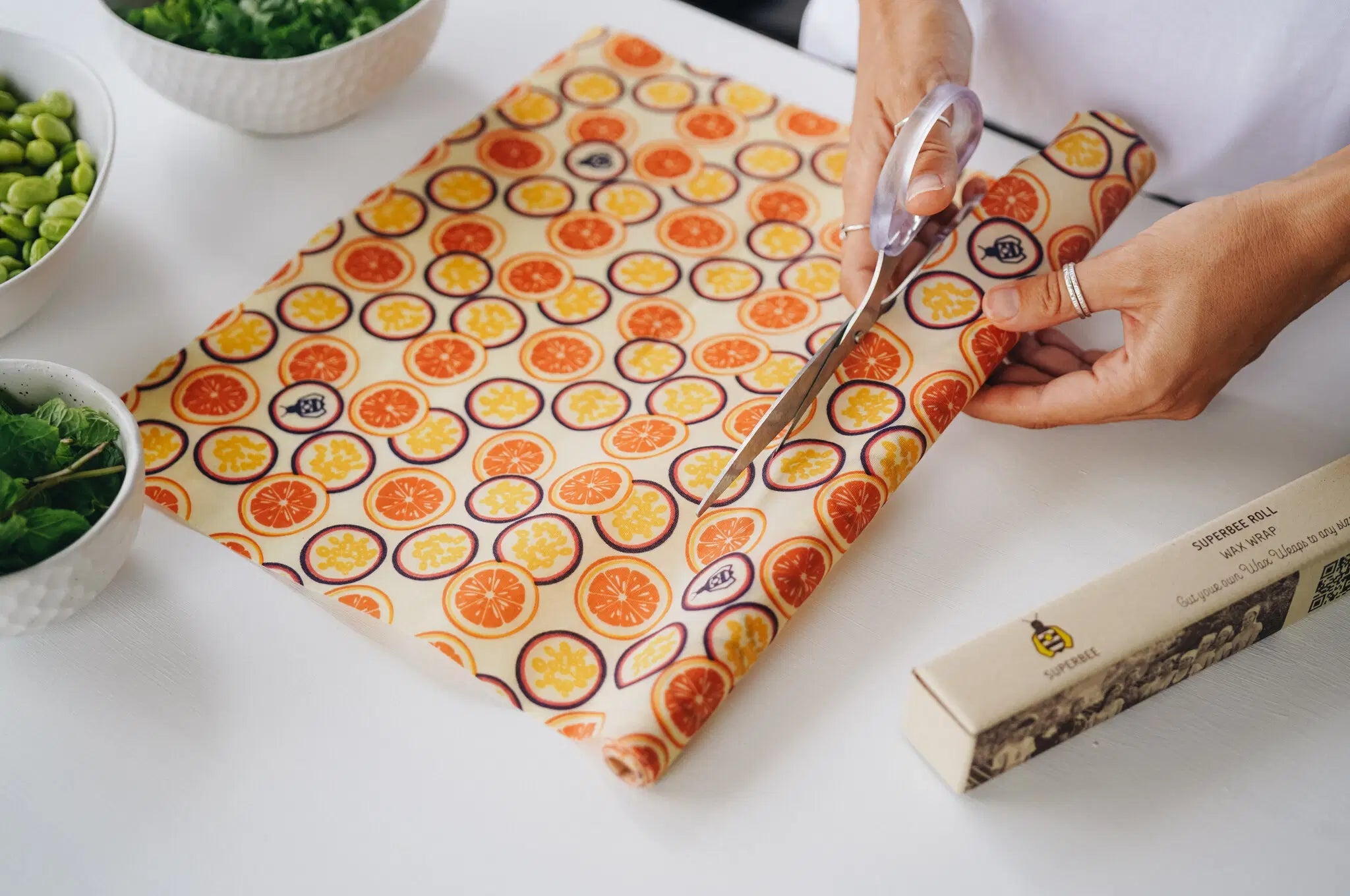 SuperBee Australia beeswax wrap roll with orange and passion fruit print being cut with scissors on a white table