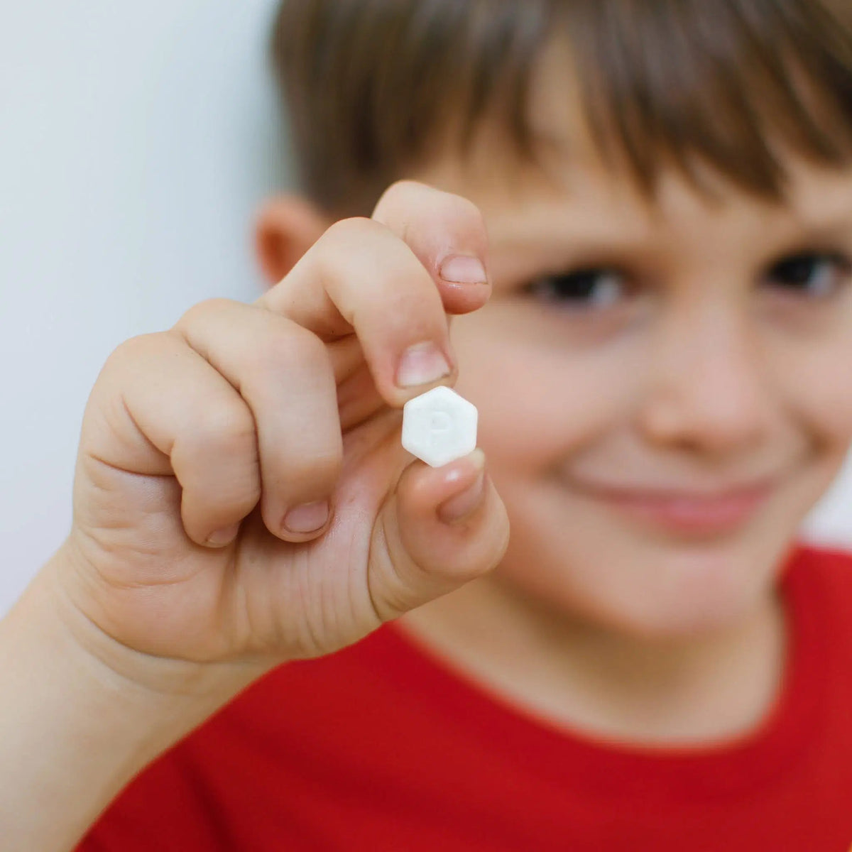 A young boy holding a white hexagonal SuperBee Australia Dentos toothpaste tablet between his fingers