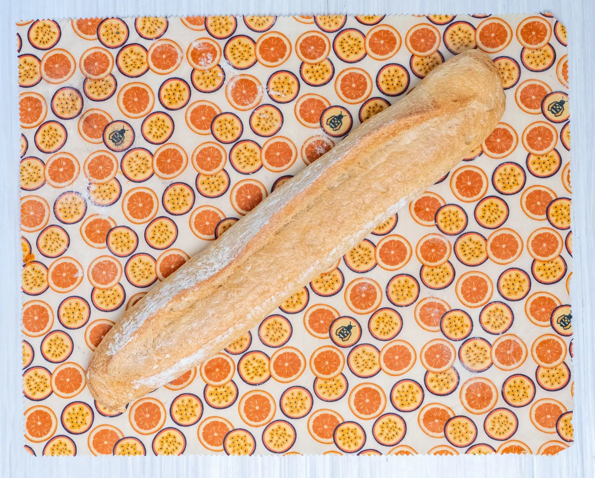 SuperBee Australia extra large beeswax wrap with a passion fruit print, holding a long crusty baguette on a table.