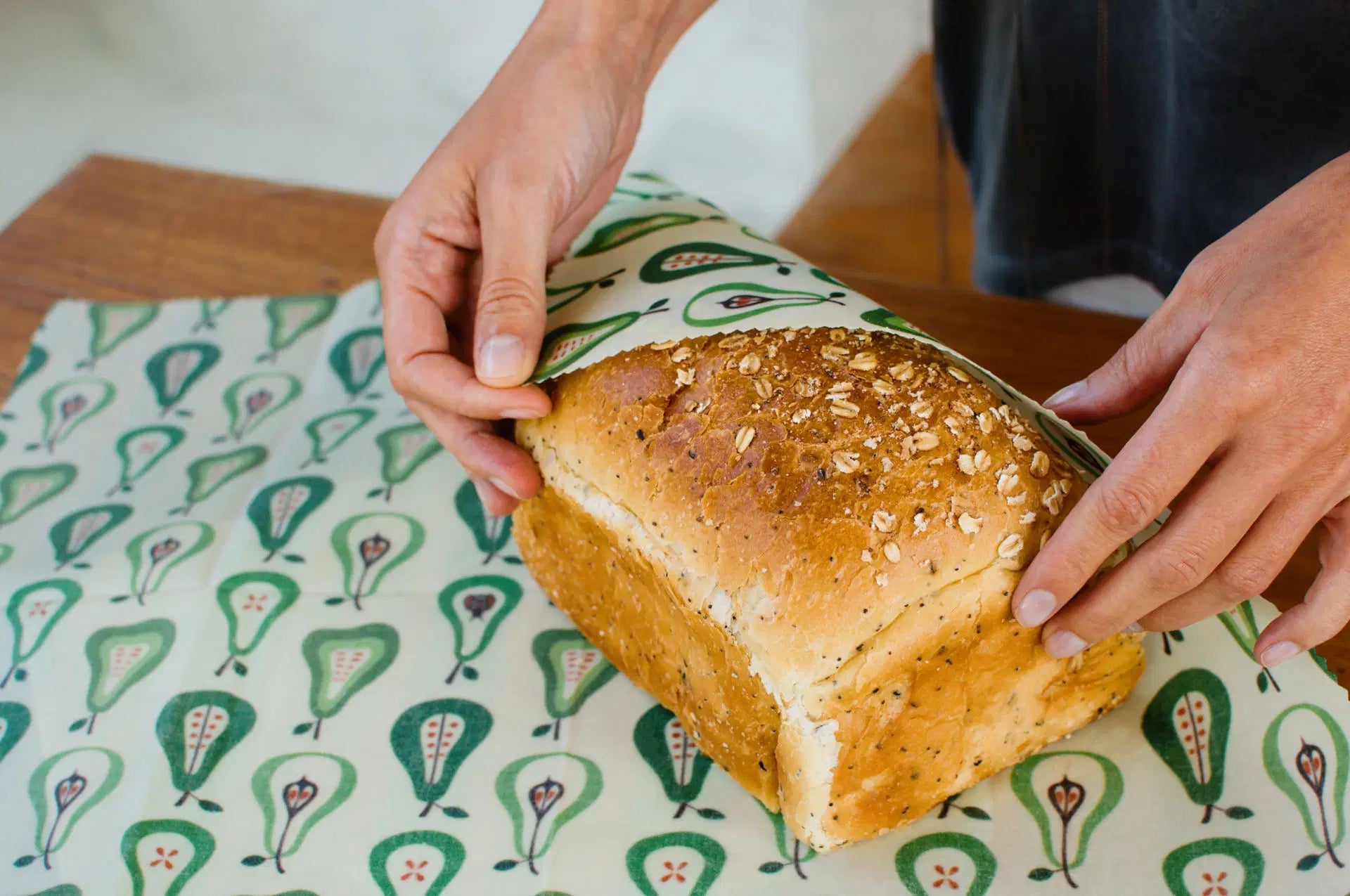 SuperBee Australia extra large beeswax wrap with a green pear pattern being used to wrap a loaf of seeded bread