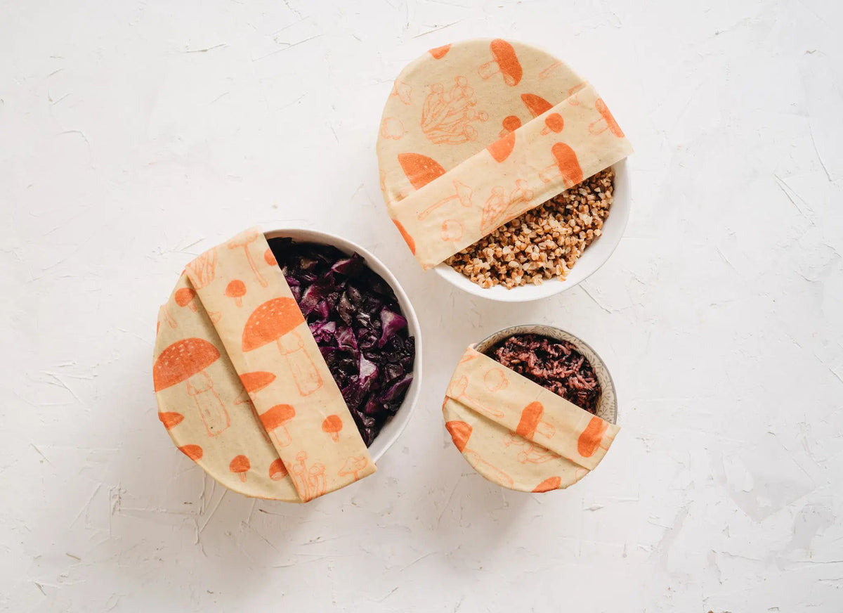 SuperBee Australia beeswax wrap roll with orange mushroom print covering three bowls of food on a white surface