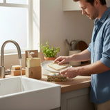Man washing a plate with a SuperBee Australia natural loofah sponge in a bright, eco-friendly kitchen.