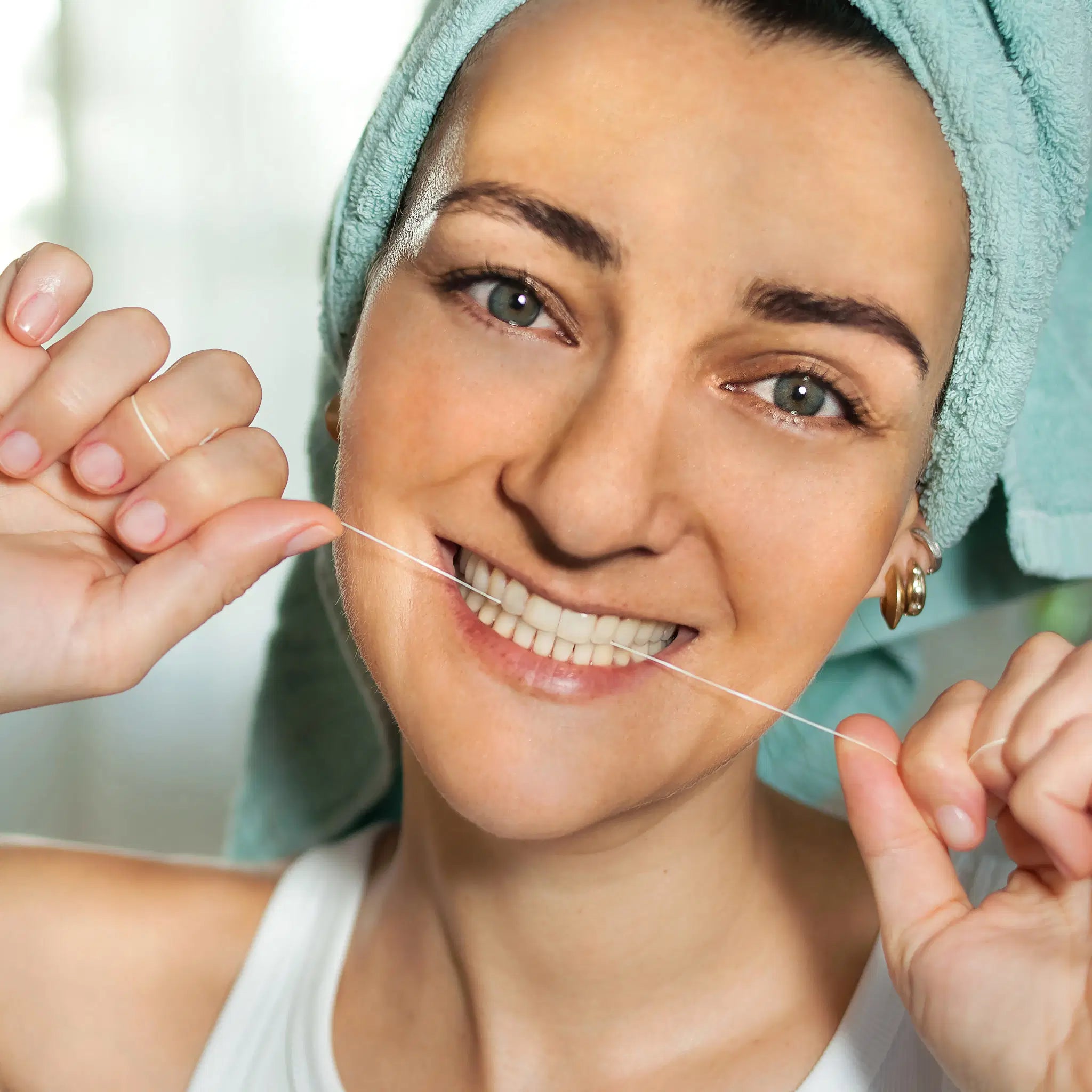 Woman with a teal hair towel using SuperBee Australia organic corn fibre dental floss for her oral care routine.