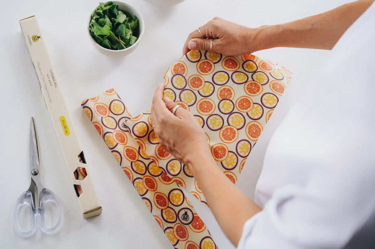 SuperBee Australia beeswax wrap roll with passion fruit print being cut to size on a white kitchen table
