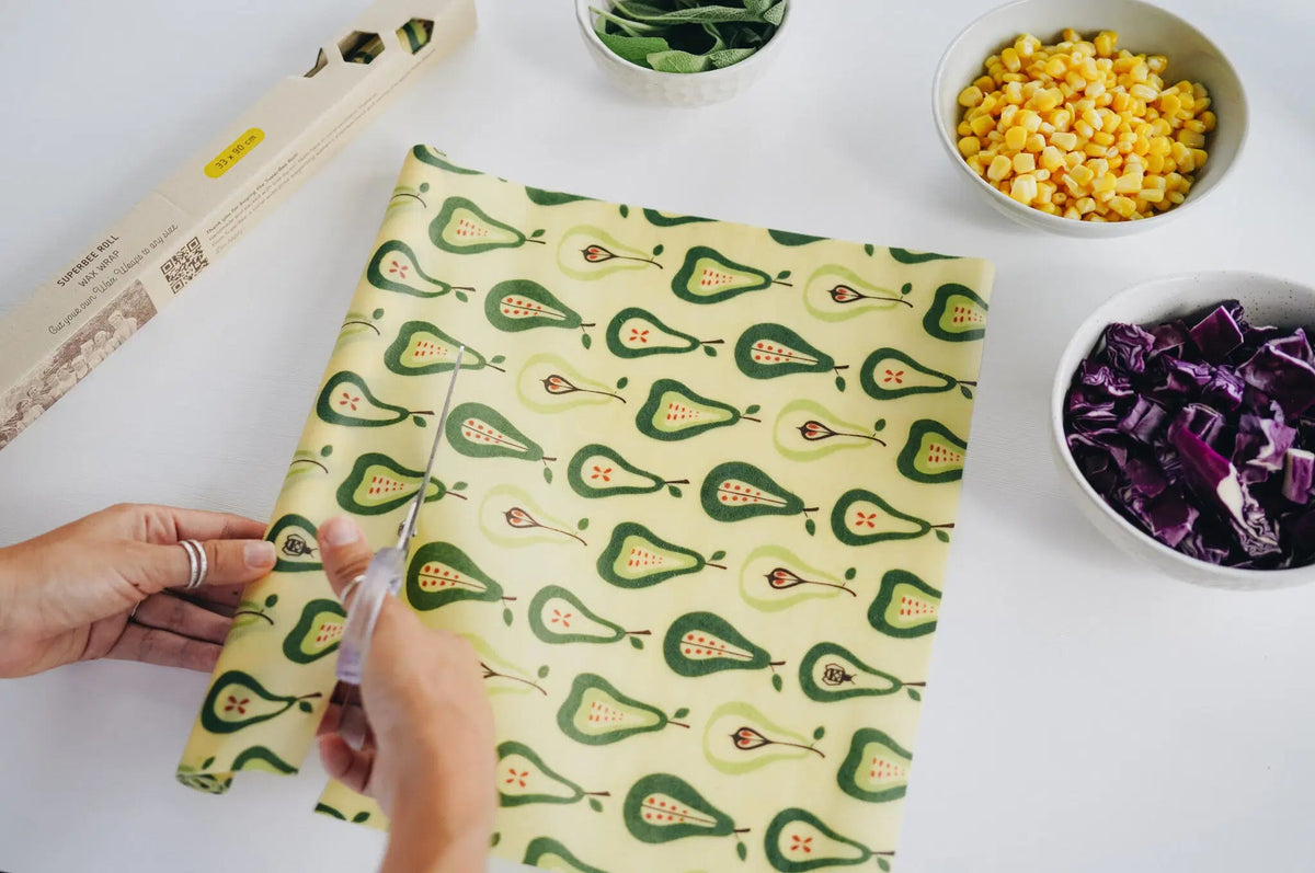 SuperBee Australia beeswax wrap roll with a green pear pattern being cut with scissors on a white kitchen table