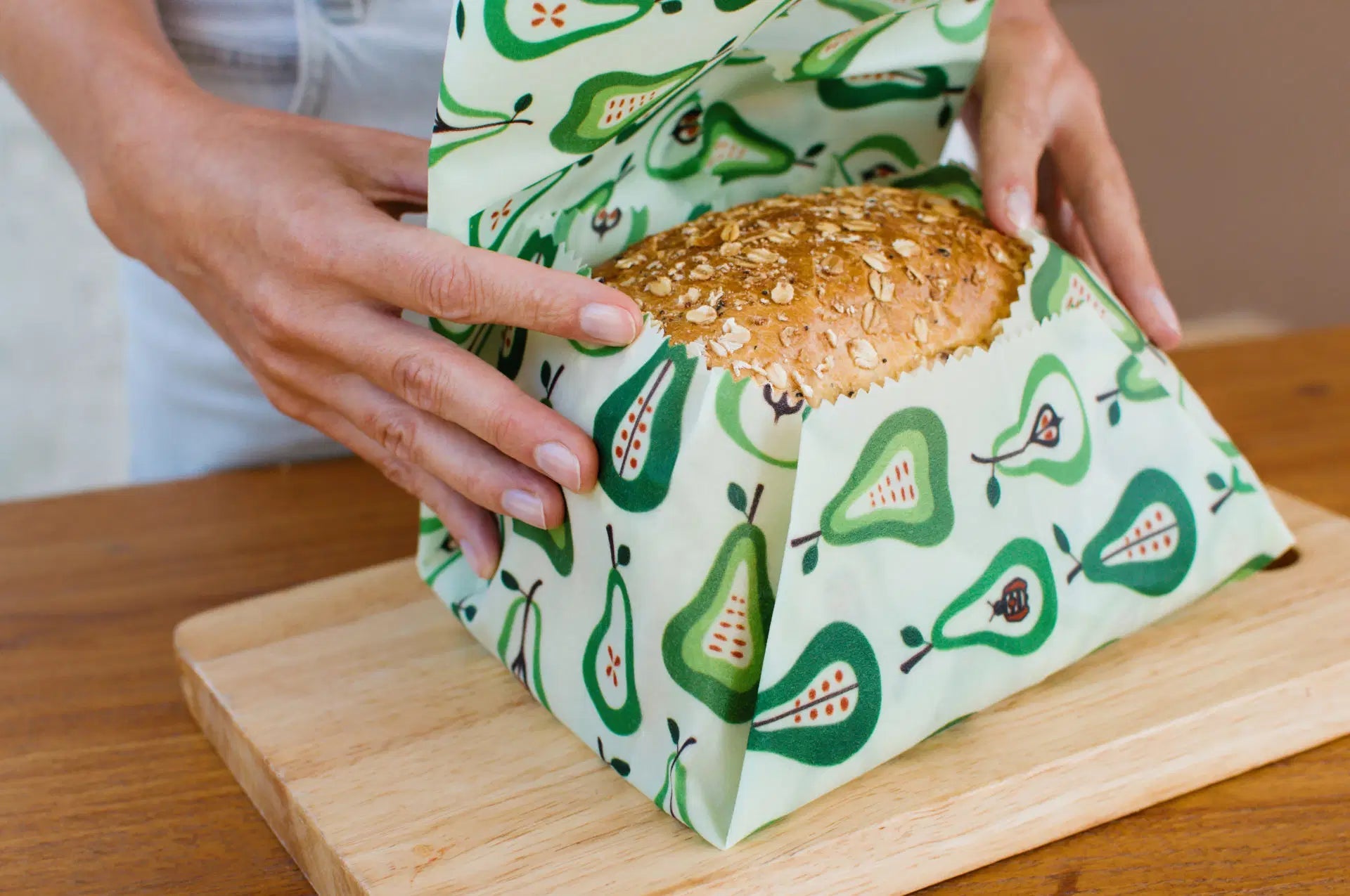 SuperBee Australia extra large reusable beeswax wrap with a green pear pattern wrapping a loaf of bread on a board.