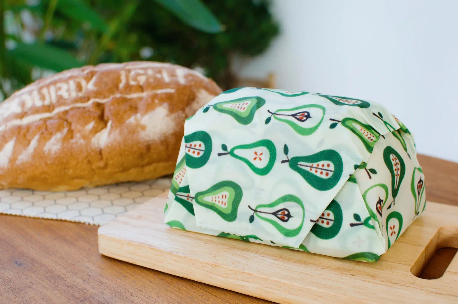 SuperBee Australia extra large reusable beeswax wrap with a green pear pattern covering a loaf of bread on a board.