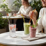 SuperBee Australia reusable borosilicate glass straws in various colors with a cleaning brush in a cafe setting.