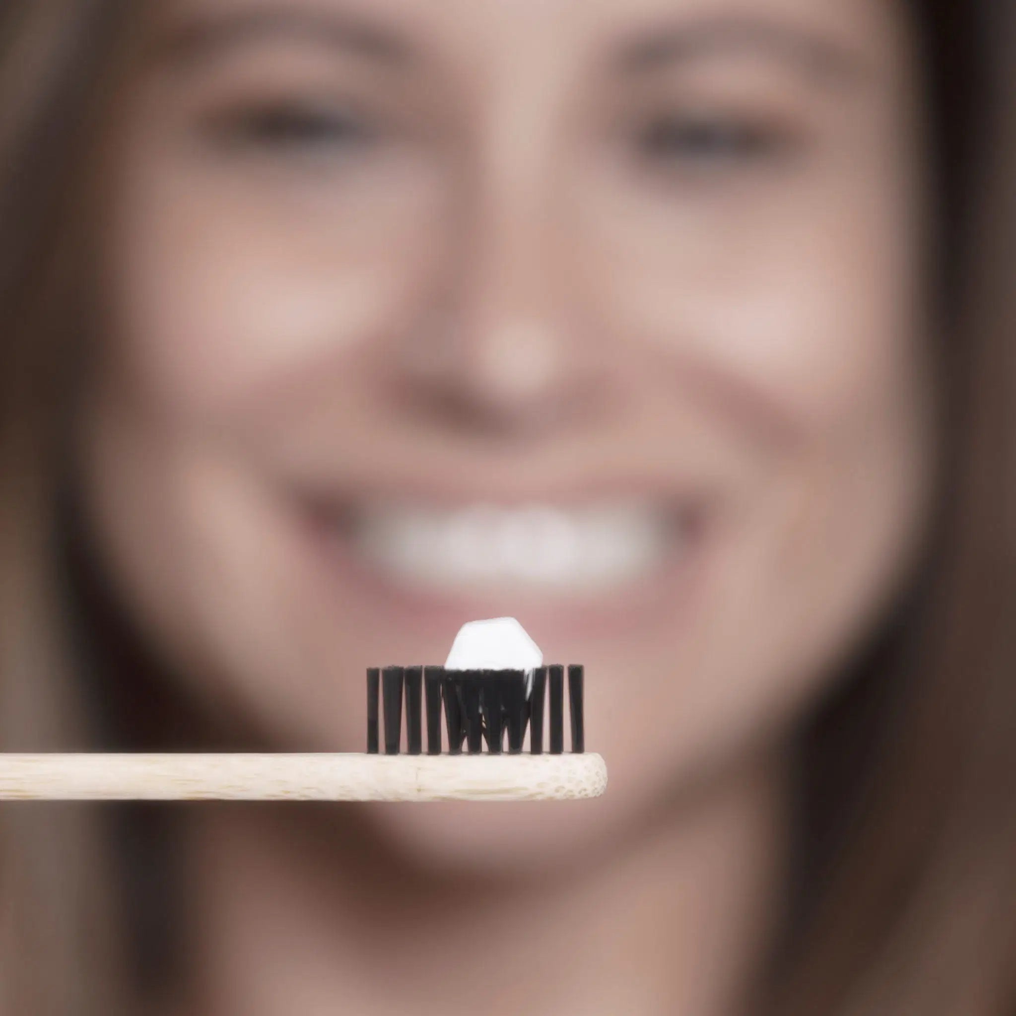 SuperBee Australia Dentos toothpaste tablet on a bamboo toothbrush with a smiling woman in the background