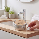 SuperBee Australia Dentos toothpaste tablet held by hand next to a reusable metal storage tin on a bathroom vanity